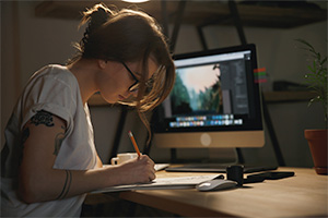 Woman drawing on a piece of paper with a computer in the background.